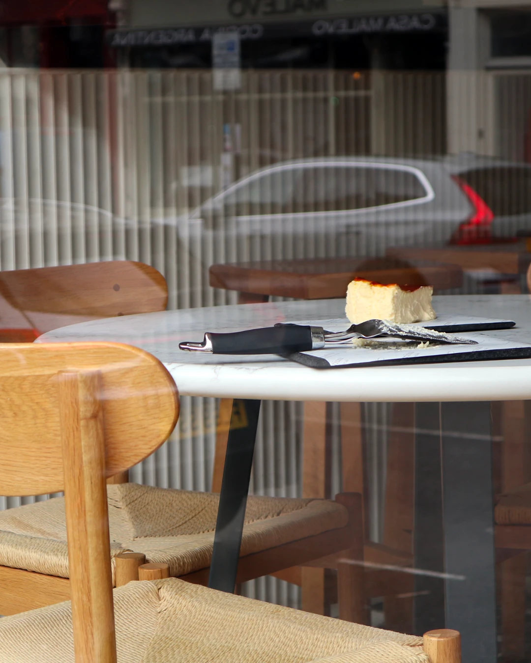 A slice of Basque cheesecake on a café table seen through the window
